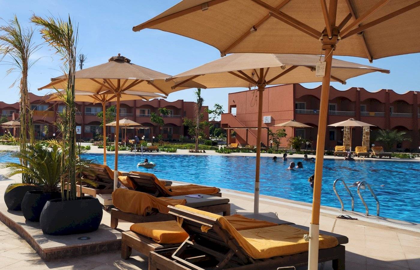 Ein Poolbereich im Three Corners Happy Life Beach Resort mit Liegestühlen und Sonnenschirmen.