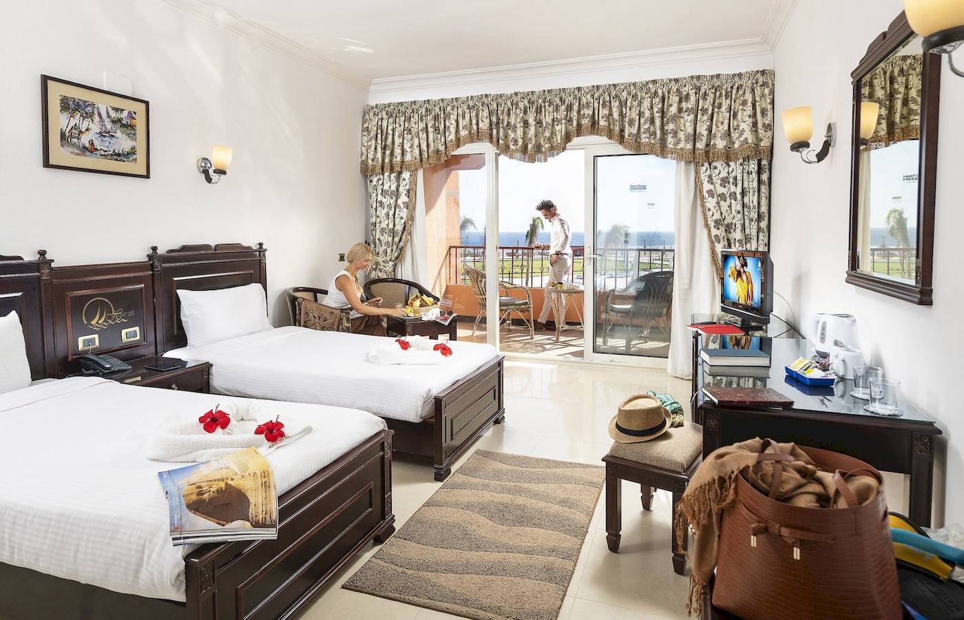 Zimmer im Three Corners Happy Life Beach Resort mit zwei Betten, einem Fernseher, einem Schreibtisch und einer Aussicht auf das Meer.