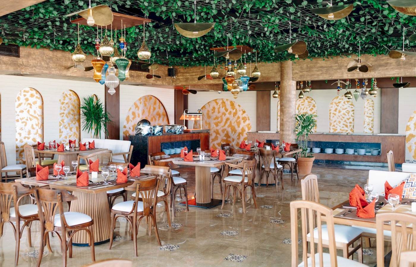 Restaurant im Three Corners Happy Life Beach Resort mit Tisch und Stühlen, geometrischen Wandmustern und dekorativen Lampen.