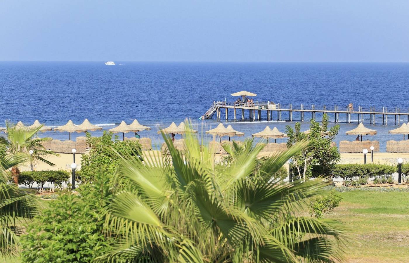 Aussicht auf das Drei Ecken Happy Leben Strand Resort mit Palmen, Strand und Pier im Hintergrund.