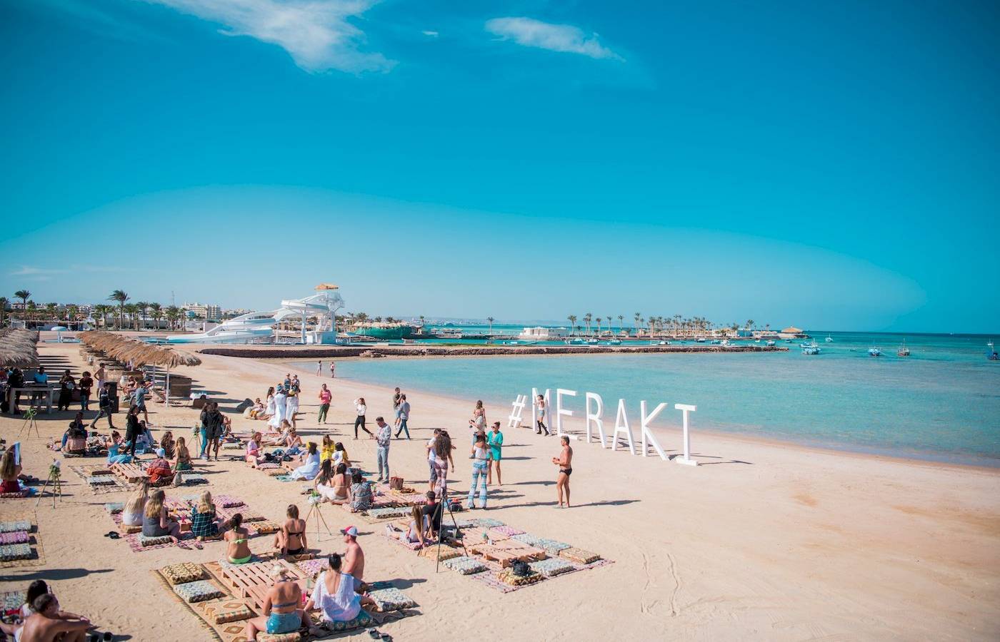 Viele Gäste auf dem Strand vor dem Sunrise Royal Makadi Resort mit großem weißen Schriftzug Merakli
