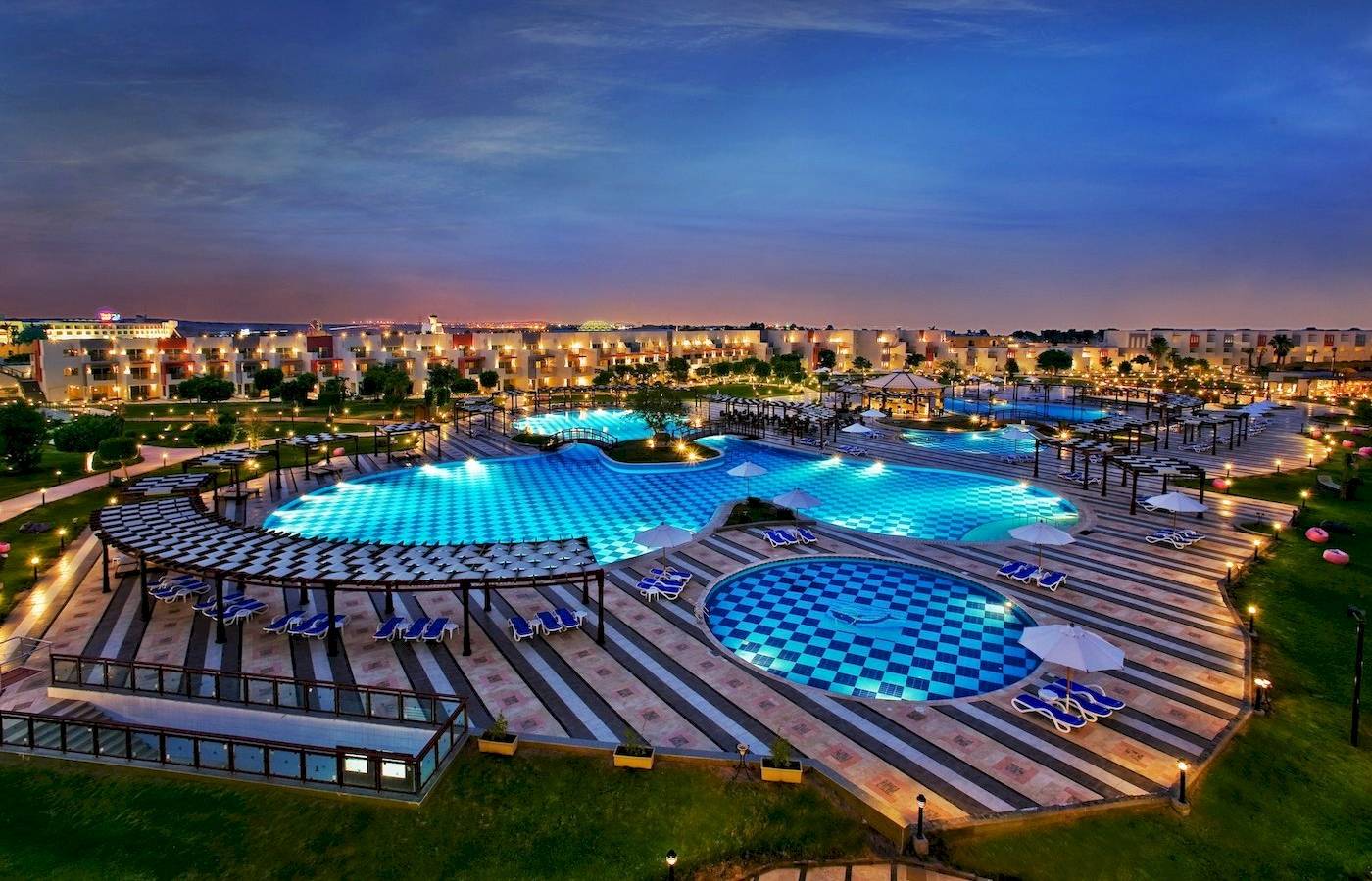 Beleuchteter Poolbereich des Sunrise Royal Makadi Resorts mit mehreren Schwimmbecken und Liegen.
