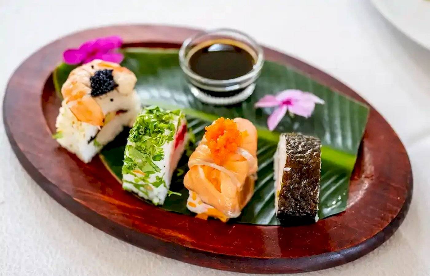 Ein Teller mit verschiedenen Sushi-Variationen auf einem Blatt serviert, mit Sojasauce.