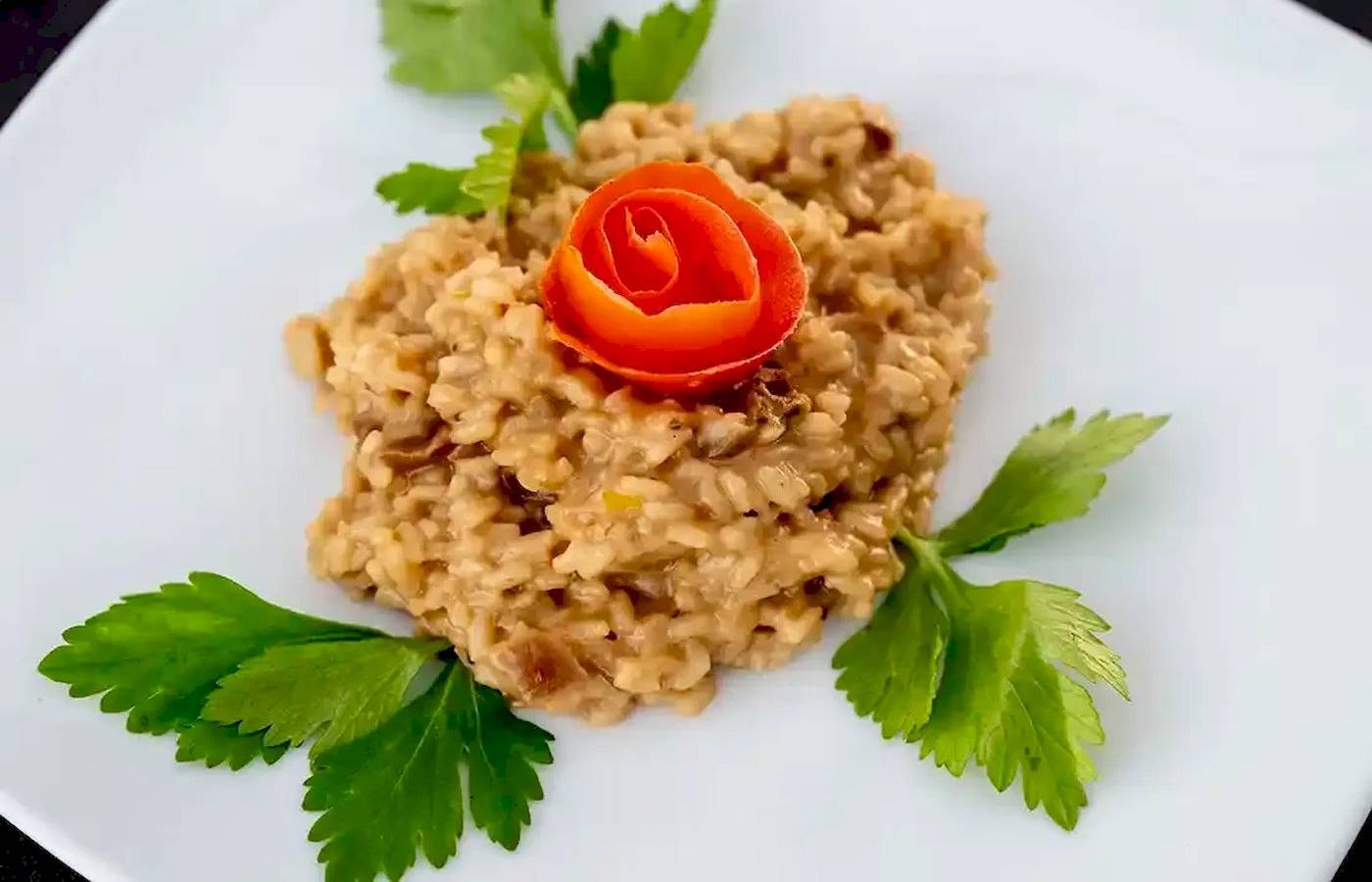 Risotto mit Pilzen und Rose auf einem weißen Teller serviert.