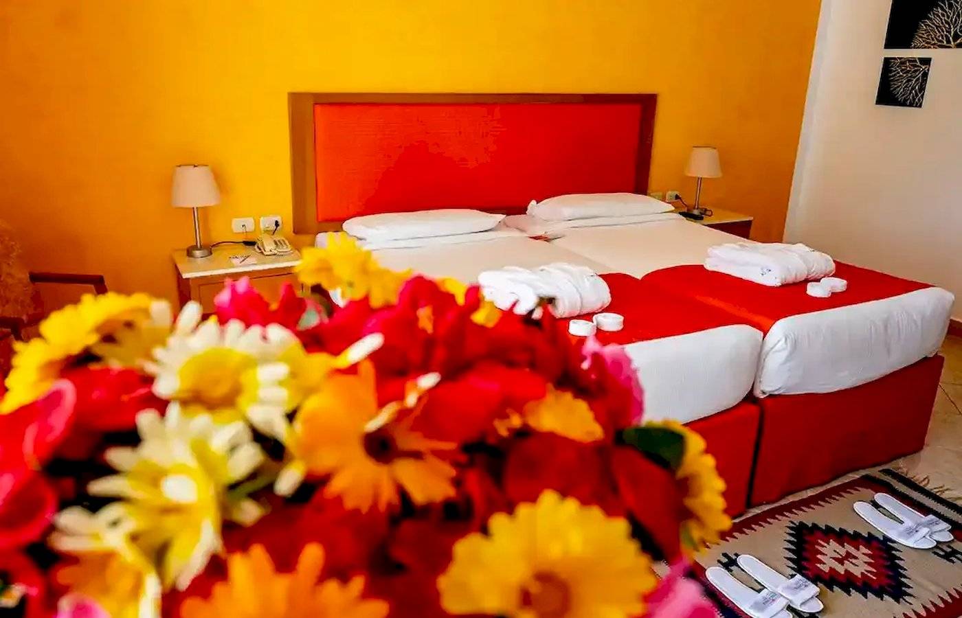Doppelzimmer im Gorgonia Beach Resort mit zwei Betten, gelben und roten Blumen, und einem roten Kopfteil.