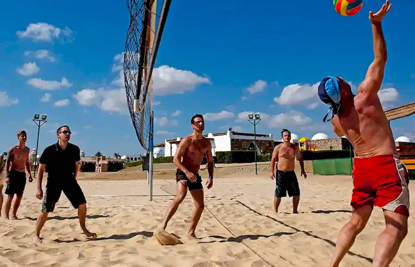 Mehrere Männer spielen Volleyball auf einem Sandstrand in der Nähe eines Hotels.