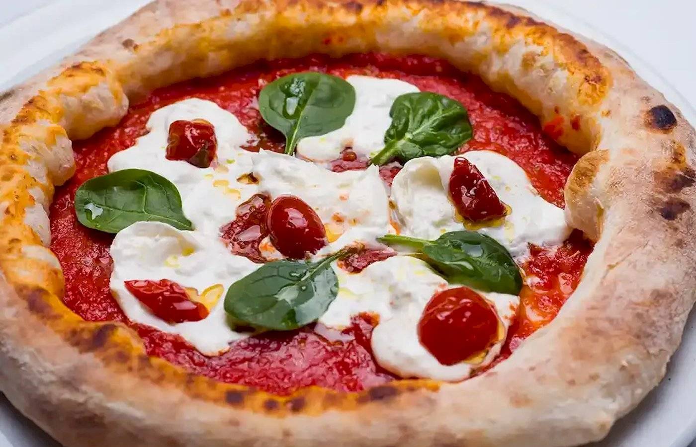 Pizza mit Mozzarella und Spinat auf einem weißen Teller serviert