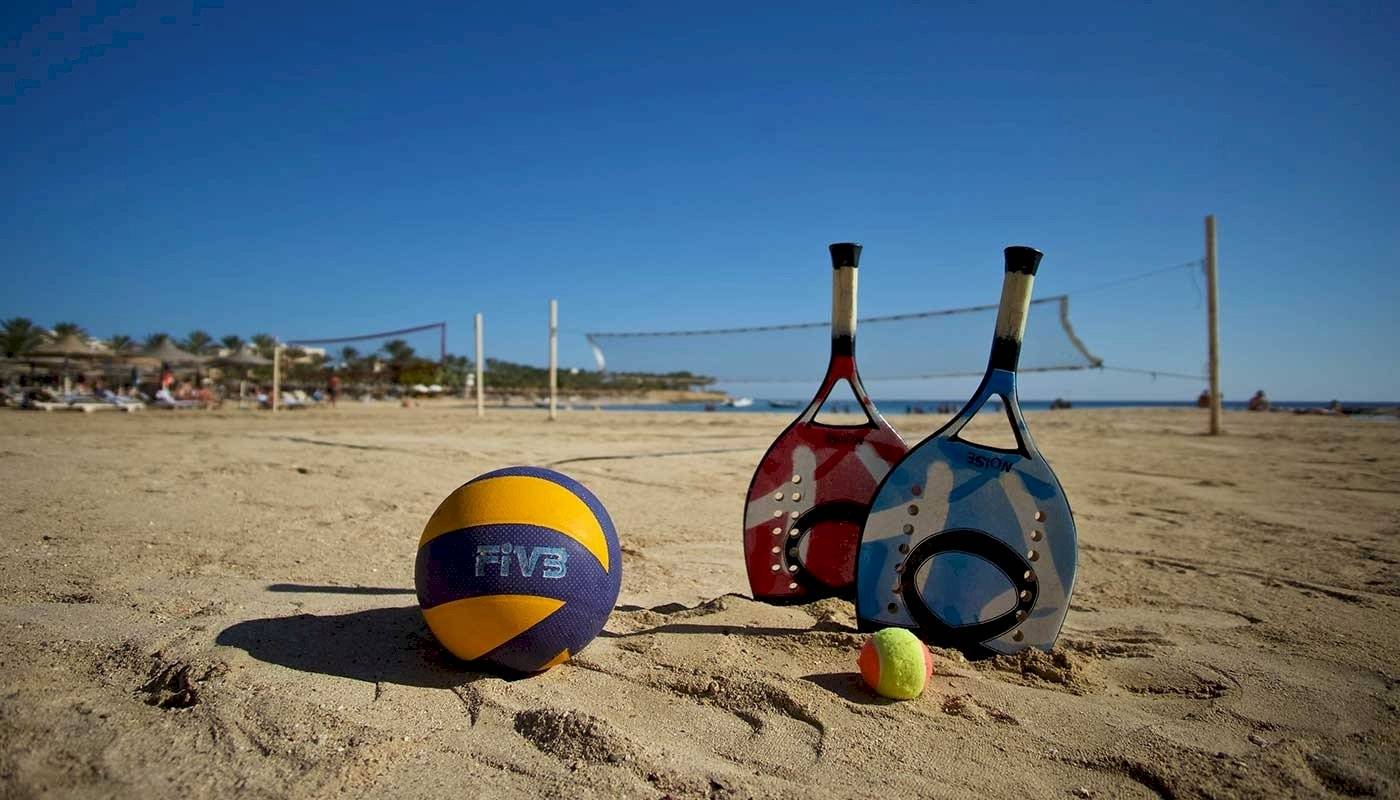 Volleyball-Ausrüstung auf einem sandigen Strand mit einem Volleyball, Tennisschläger und einem Tennisball.