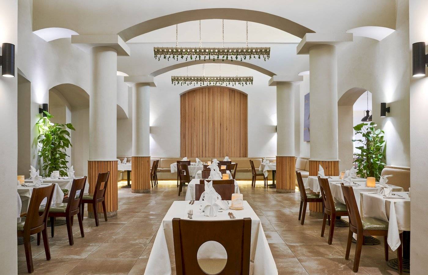 Innenansicht des Restaurants im Three Corners Rihana Resort mit Tisch und Stühlen, weißen Tischdecken, dekorativen Pflanzen und Holzelementen.