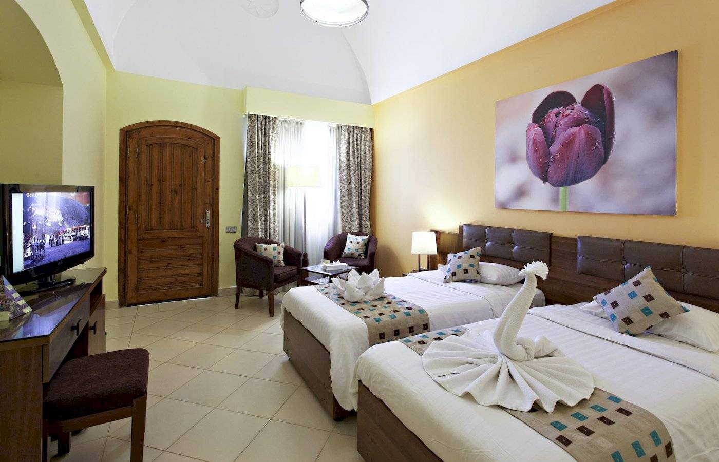 Innenansicht eines Doppelzimmers im Three Corners Rihana Resort mit zwei Betten, Fernseher, Dekor und Möbeln.