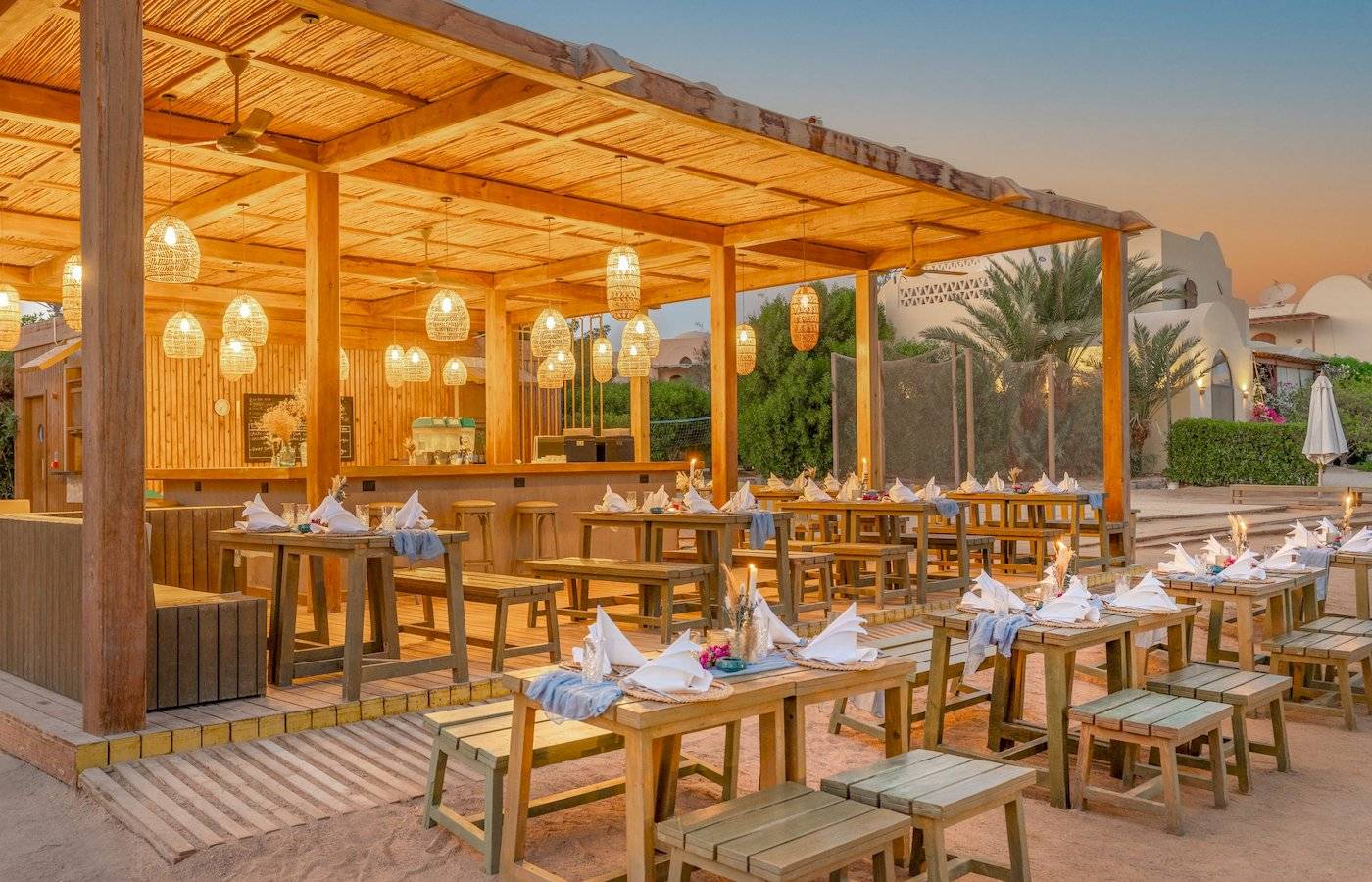 Strandrestaurant des Three Corners Rihana Resorts mit Holztischen und Stühlen, unter einem Strohdach mit Kerzen und Laternen.