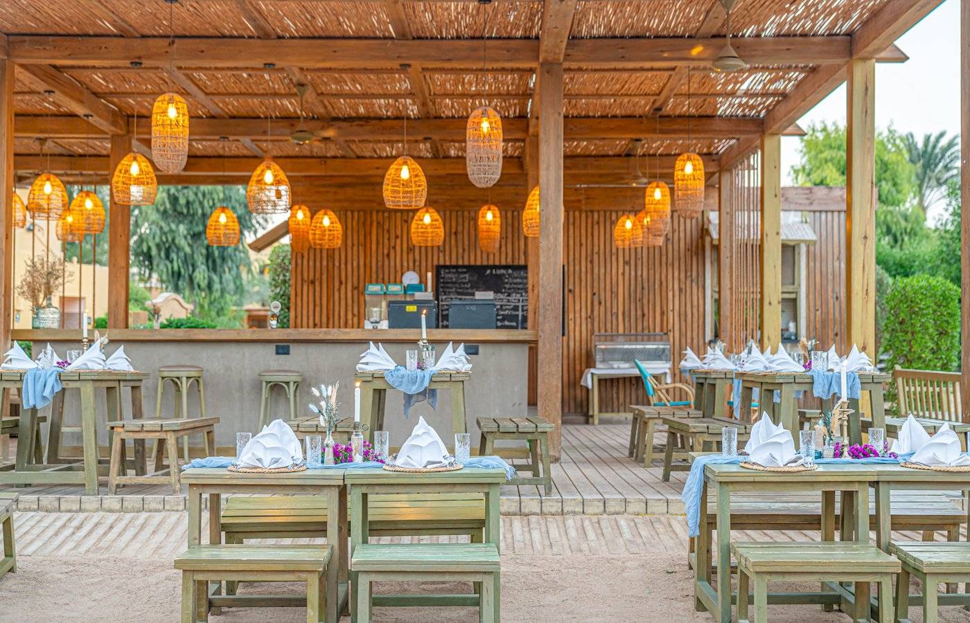 Terrasse des Three Corners Rihana Resorts mit bestuhlten Tischen und hölzerner Überdachung.