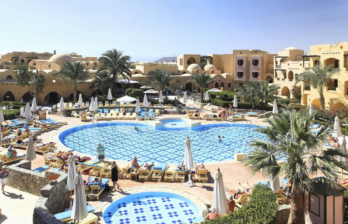 Dreieckiges Ecken Rihana Resort Pool mit Liegen, Sonnenschirmen und Palmen