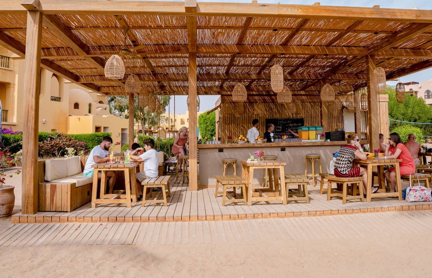 Gäste sitzen an Tischen im Freien unter einem Holzpavillon im Three Corners Rihana Resort.