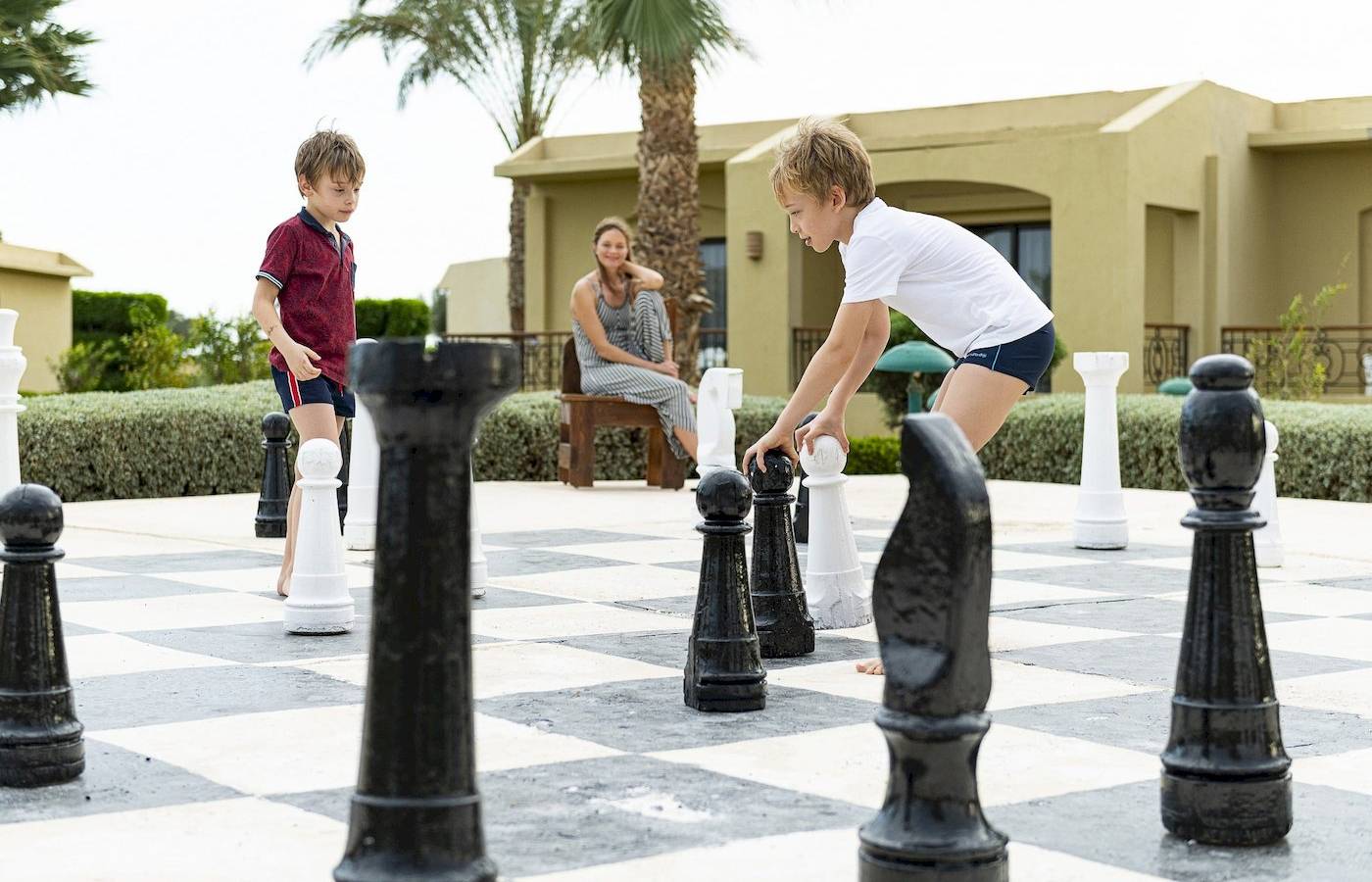 Zwei Kinder spielen Schach im Freien neben einem Hotel.
