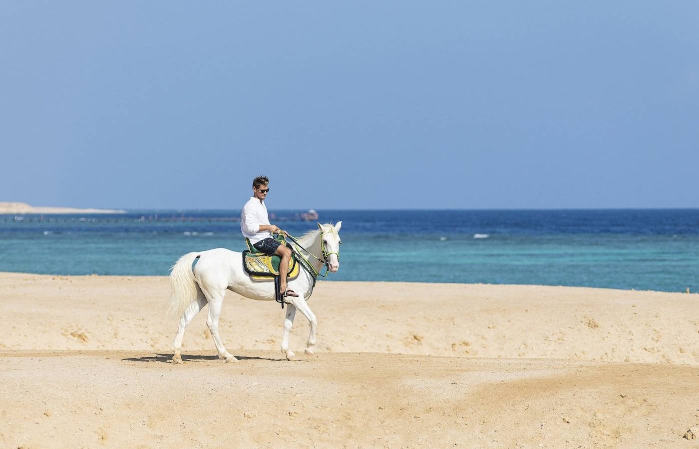 Ein Mann reitet auf einem weißen Pferd auf dem Strand des Three Corners Fayrouz Plaza Beach Resort.