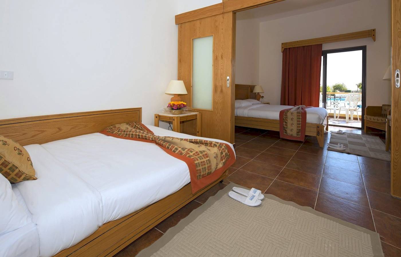 Zwei Betten im Zimmer des Three Corners Fayrouz Plaza Beach Resort mit einem offenen Fenster und Blick auf die Terrasse.