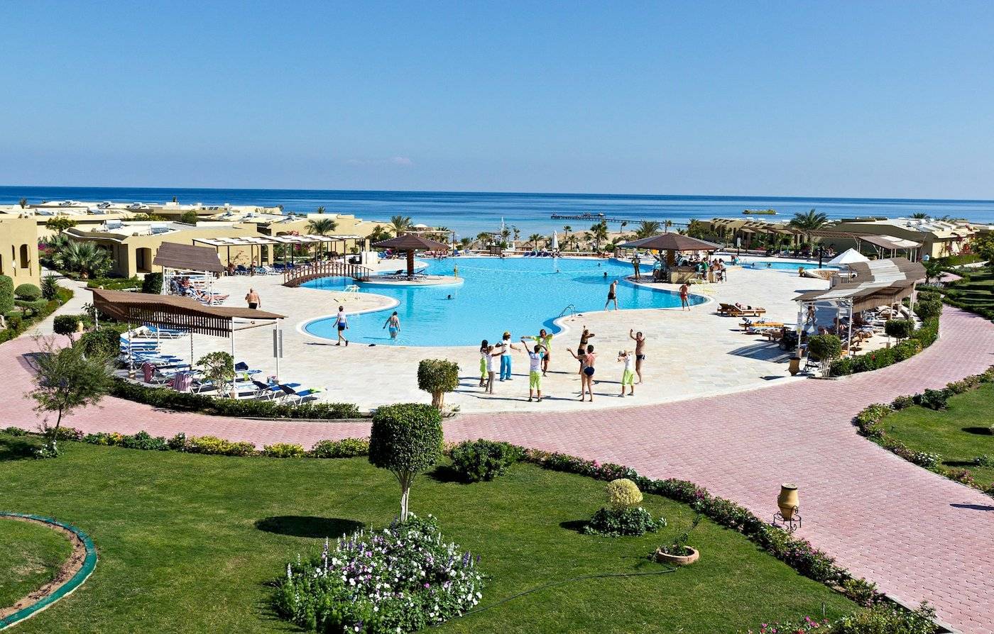 Luftaufnahme des Swimmingpools im Three Corners Fayrouz Plaza Beach Resort mit Gästen, Sonnenliegen und Palmen.