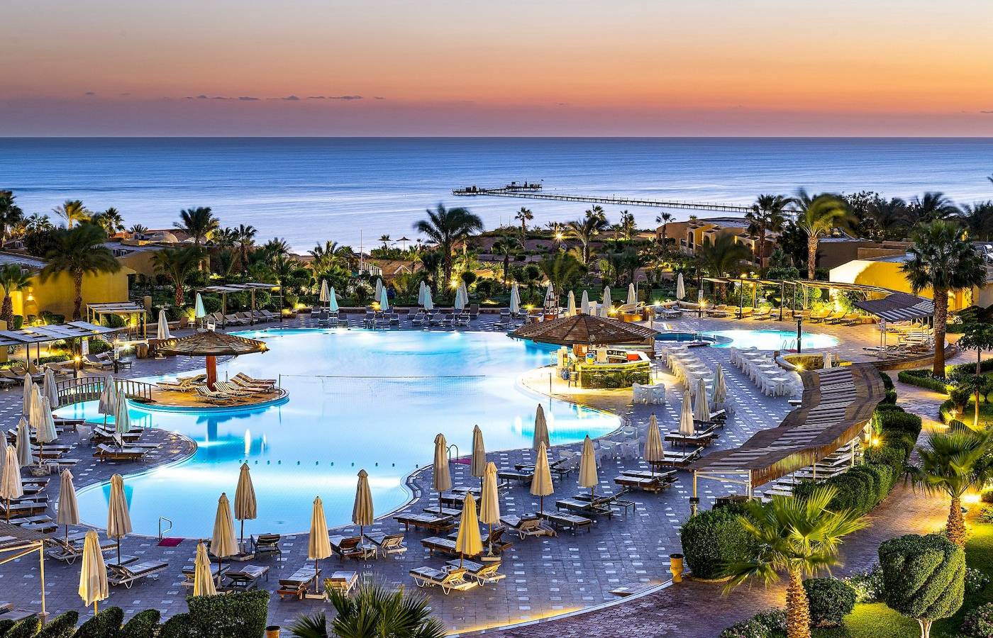 Drei-Ecken-Fayrouz-Plaza-Strandresort-Pool-Bereich mit blauem Wasser und Sonnenuntergang.