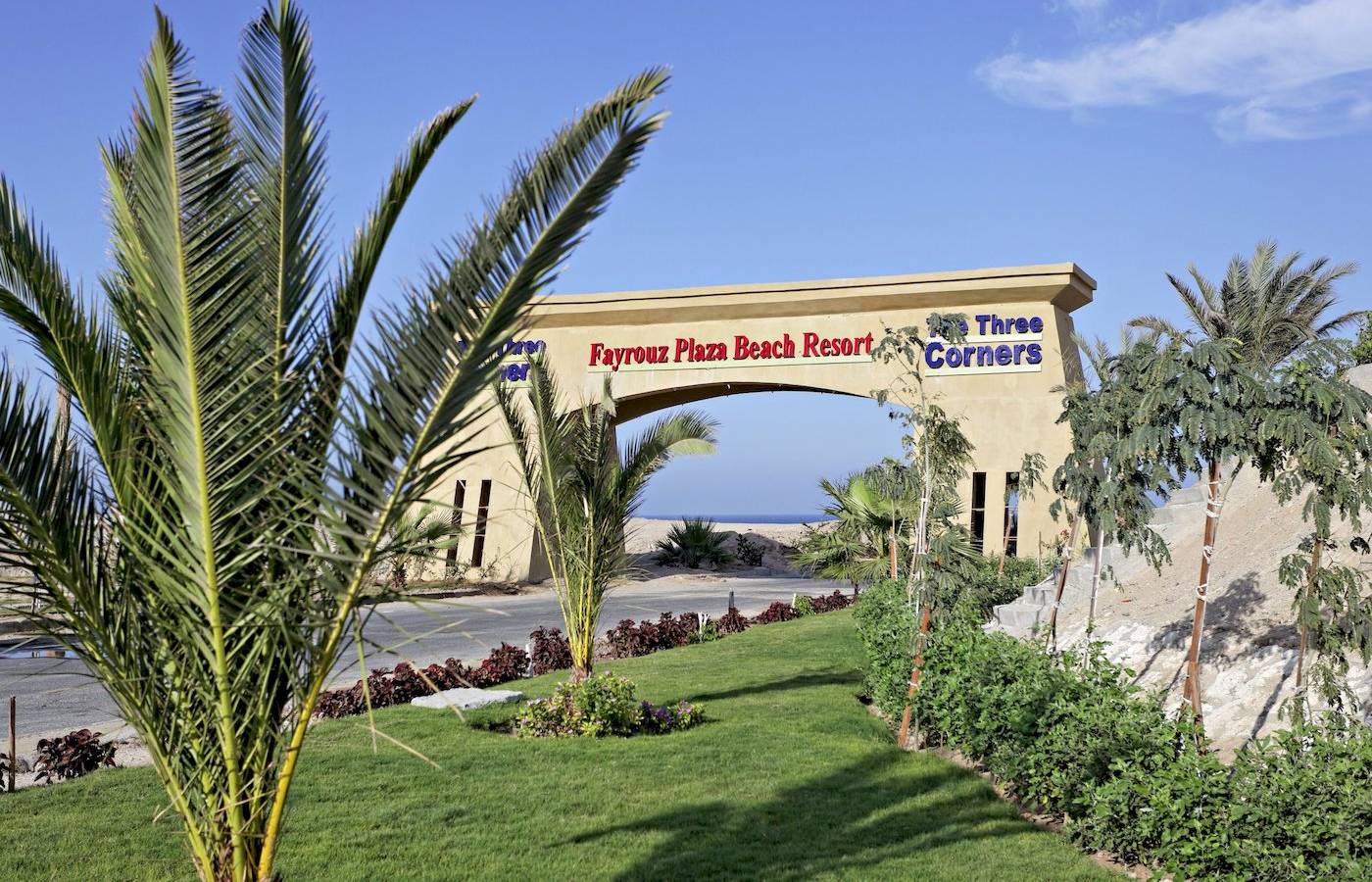 Eingang zum Three Corners Fayrouz Plaza Beach Resort mit Palmen und Rasen im Vordergrund.
