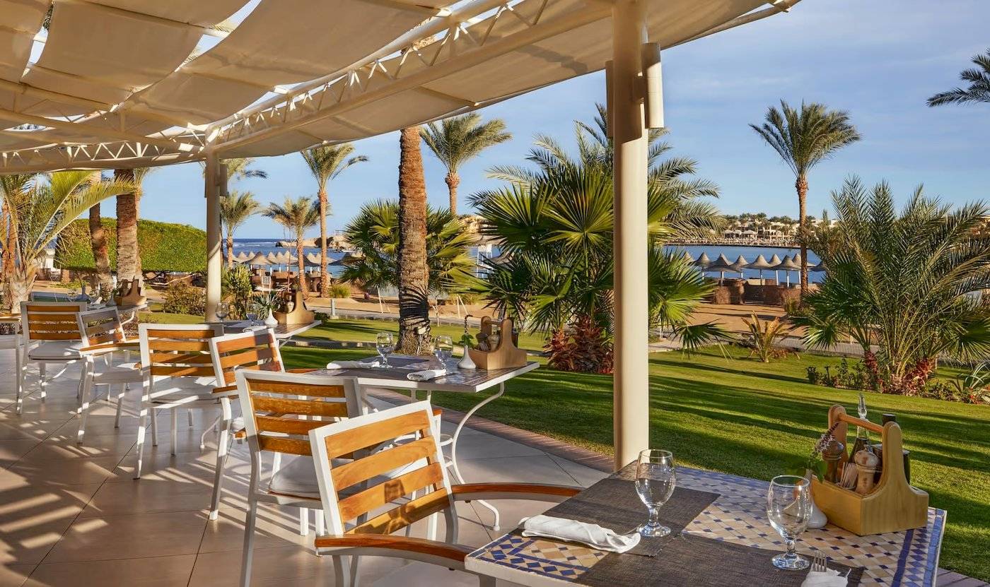 Außenterrasse des Steigenberger Coraya Beach Hotels mit Tischen und Stühlen, umgeben von Palmen und Meerblick.