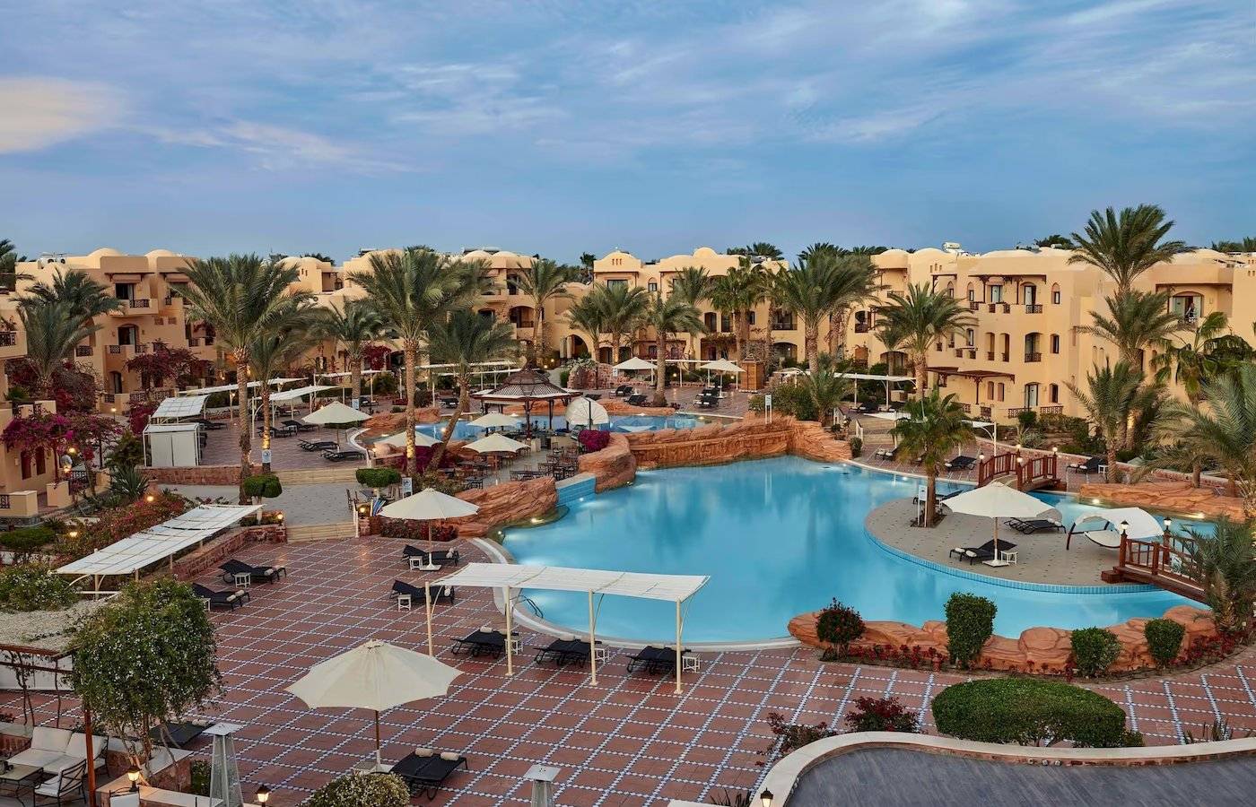 Außenbereich des Steigenberger Coraya Beach Hotels mit Swimmingpool, Liegestühlen und Palmen.
