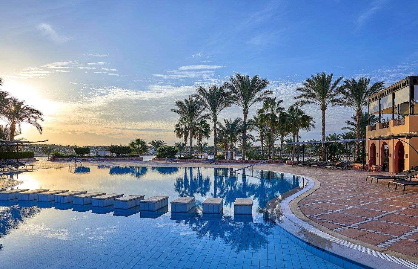 Außenpool des Steigenberger Coraya Beach Hotels bei Sonnenuntergang mit Palmen und Sonnenliegen.