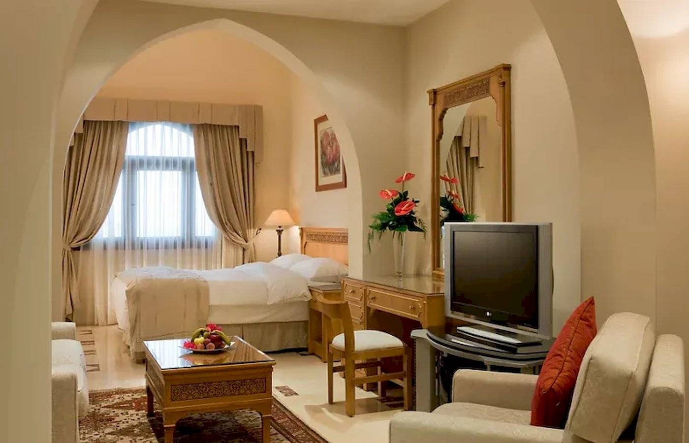 Innenansicht eines luxuriösen Zimmers im Mövenpick Resort Sharm el Sheikh mit einem Doppelbett, Fernseher, Schreibtisch, Sofa und Fenster.