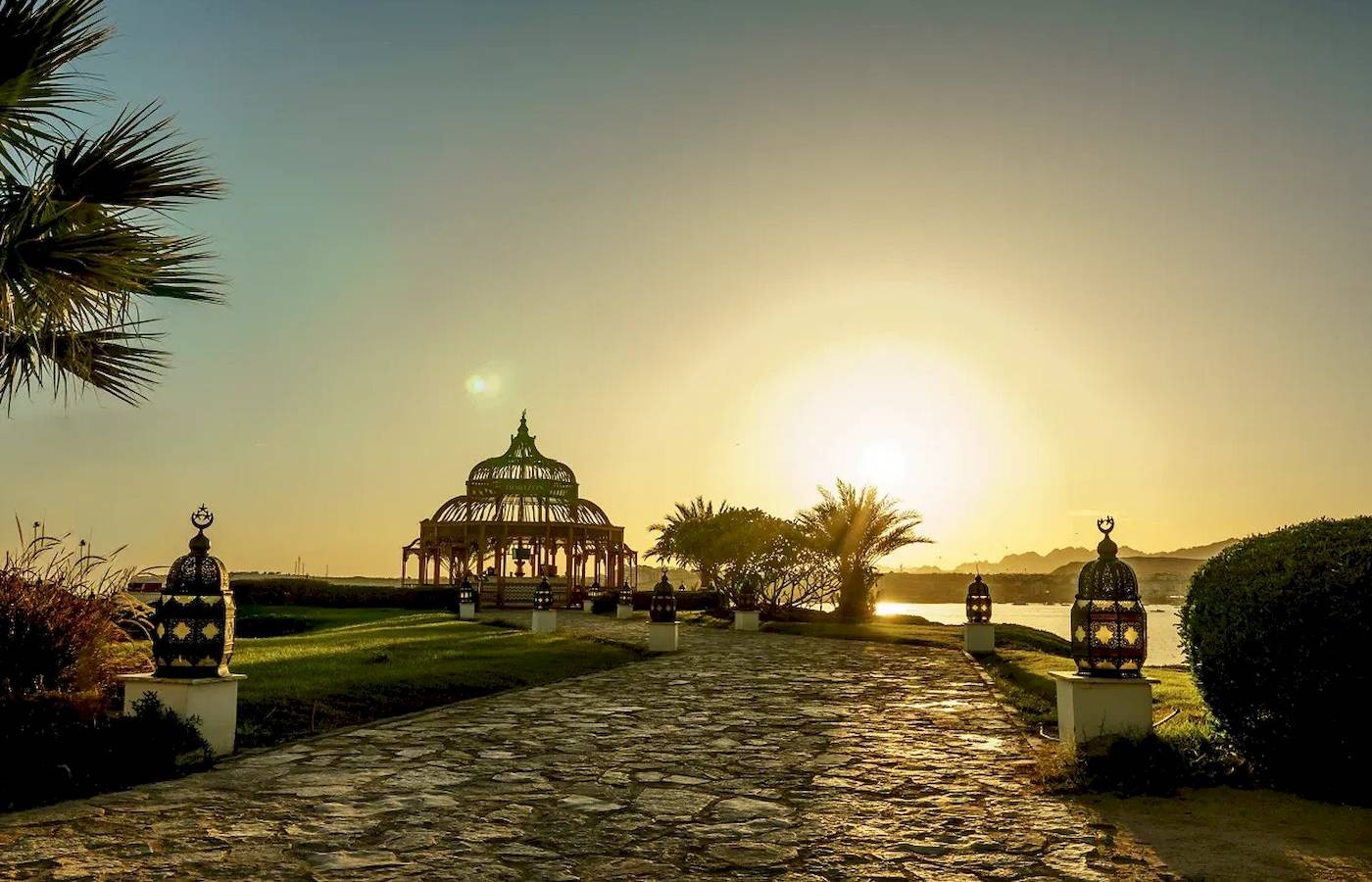 Sonnenuntergang am Mövenpick Resort Sharm el Sheikh mit einem Steinweg und Pavillon im Vordergrund.