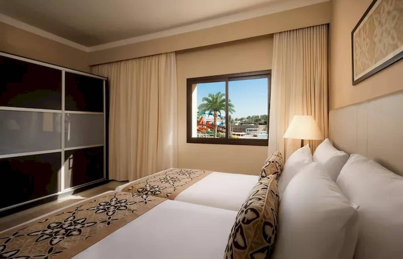 Hotelzimmer im JAZ Neo Dar El Madina mit zwei Betten, Fenster und Ausblick auf Wasserrutschen.