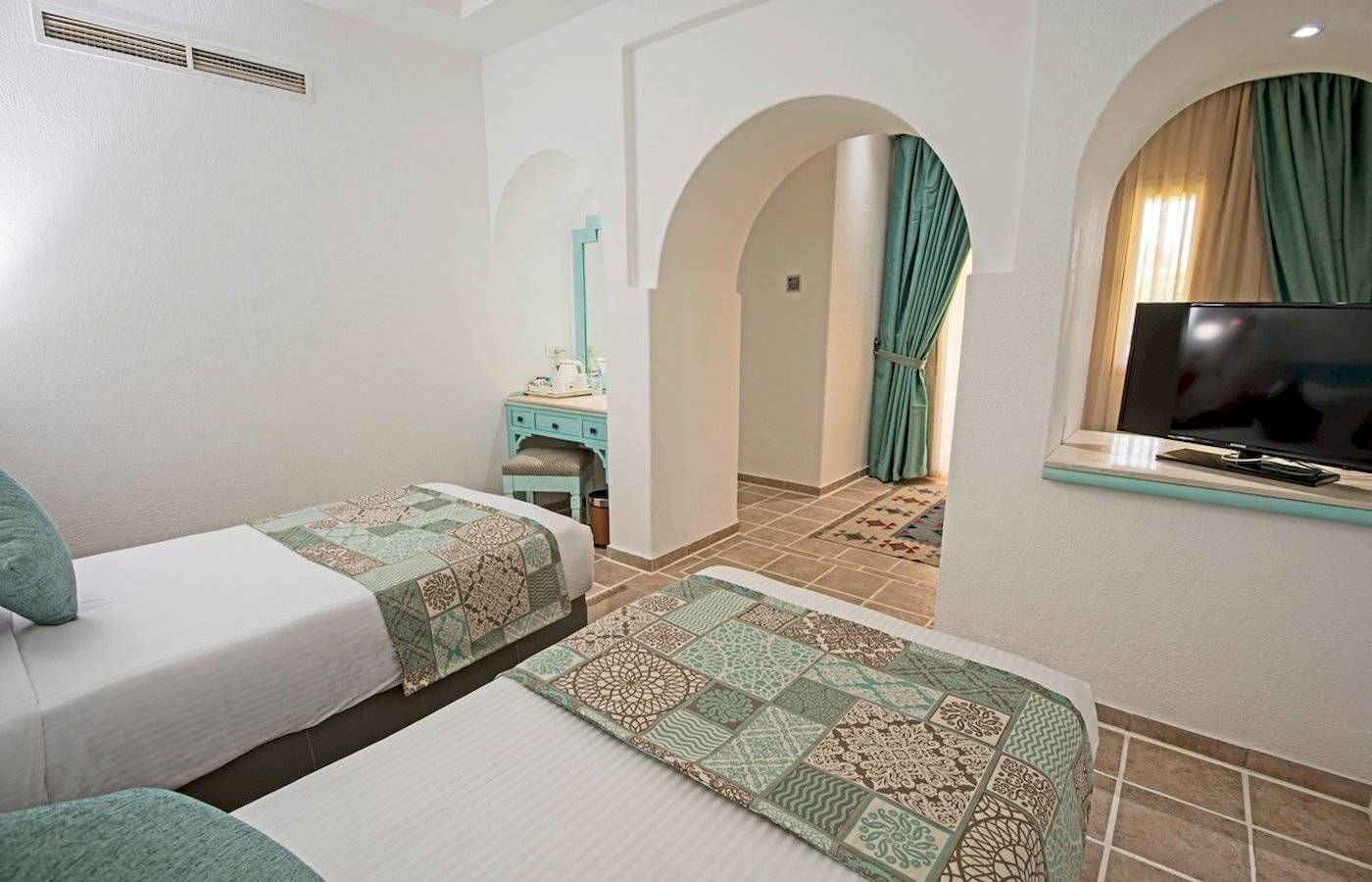Zwei Doppelbetten mit blauen Kissen in einem eleganten Zimmer des Sunrise Royal Makadi Resorts.