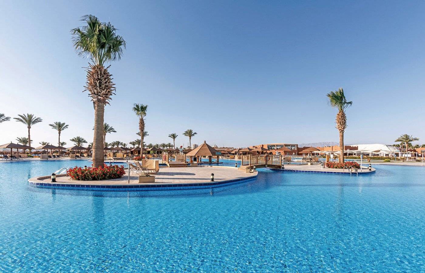 Außenpool des Sunrise Royal Makadi Resorts mit Palmen und Gebäuden im Hintergrund.