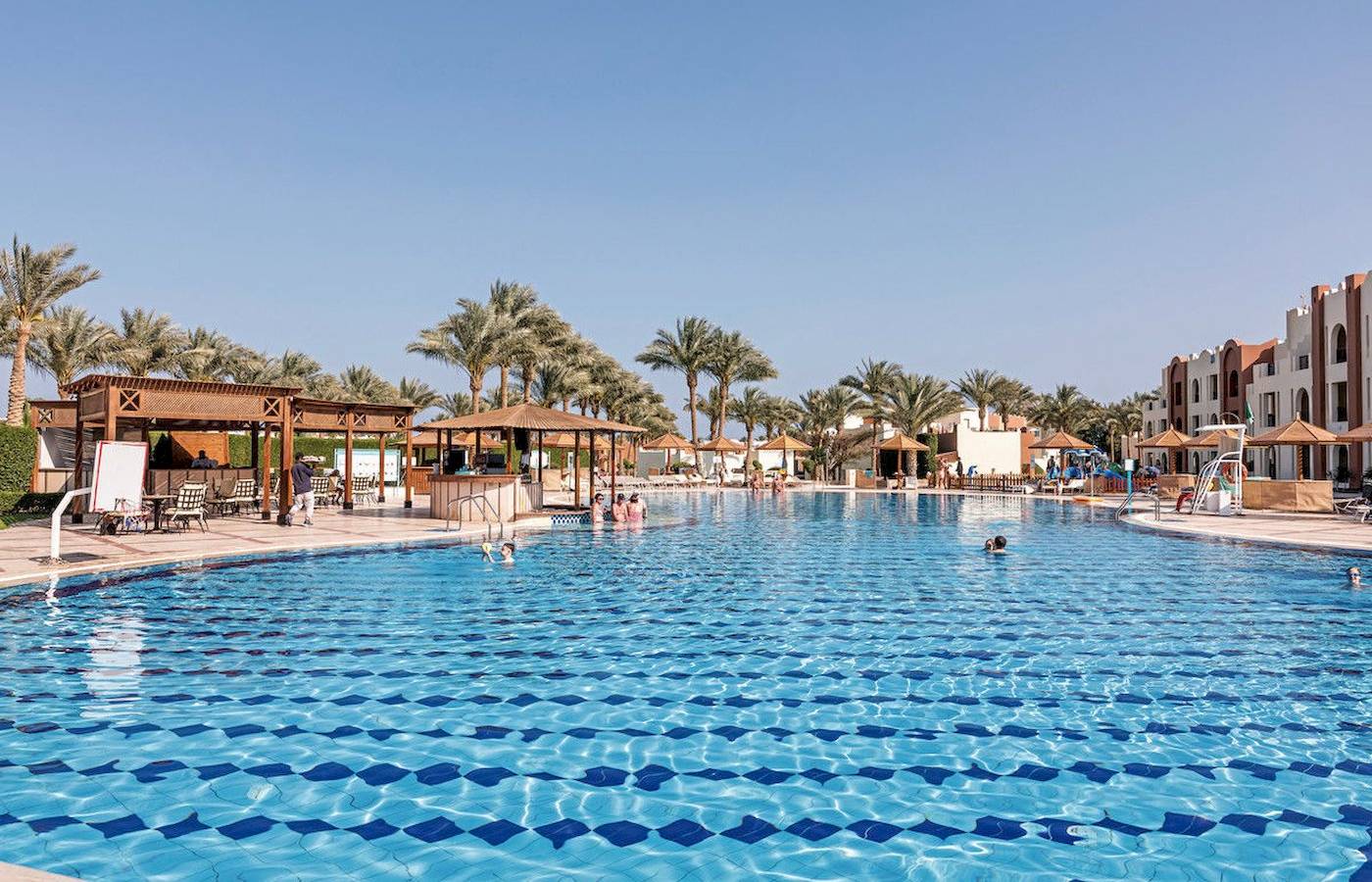 Außenpool im SUNRISE Royal Makadi Resort mit mehreren Schwimmern und Sonnenschirmen.