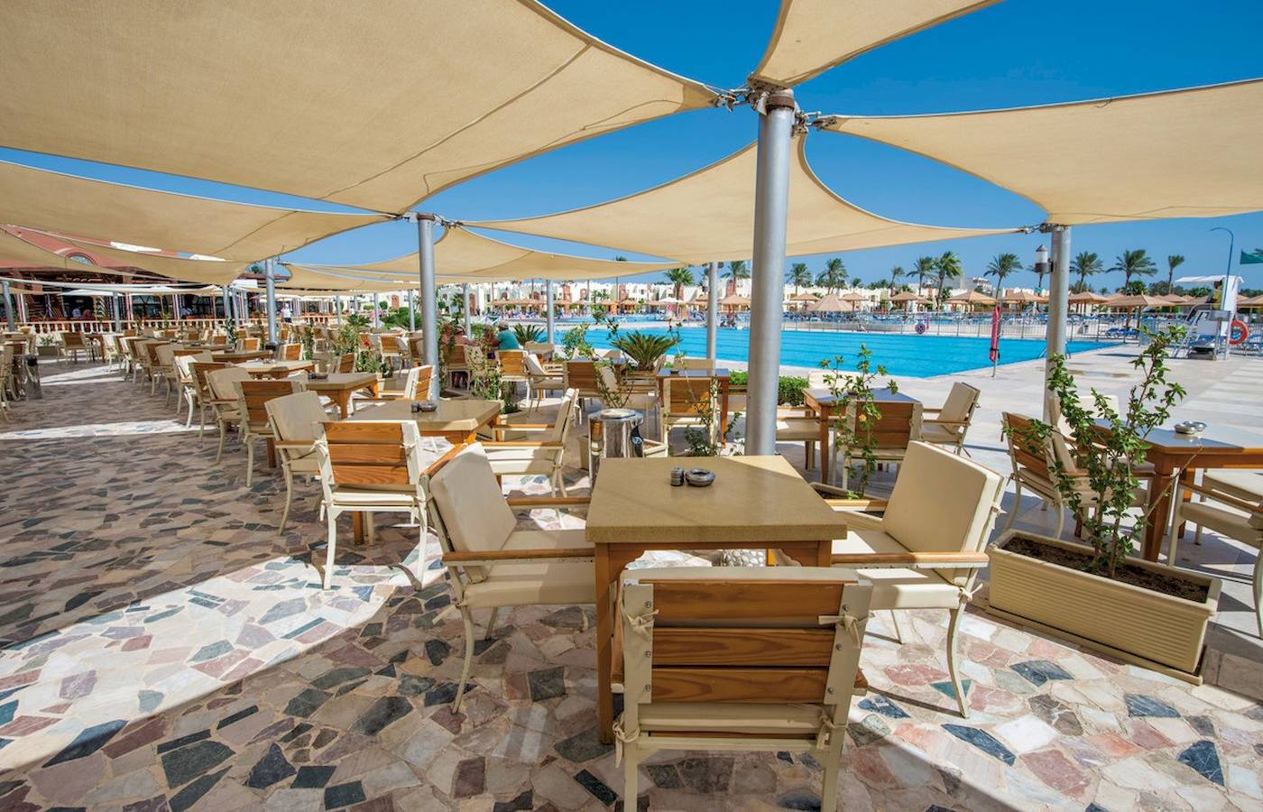 Außenbereich des Sunrise Royal Makadi Resorts mit Tischen, Stühlen und Sonnenschirmen.