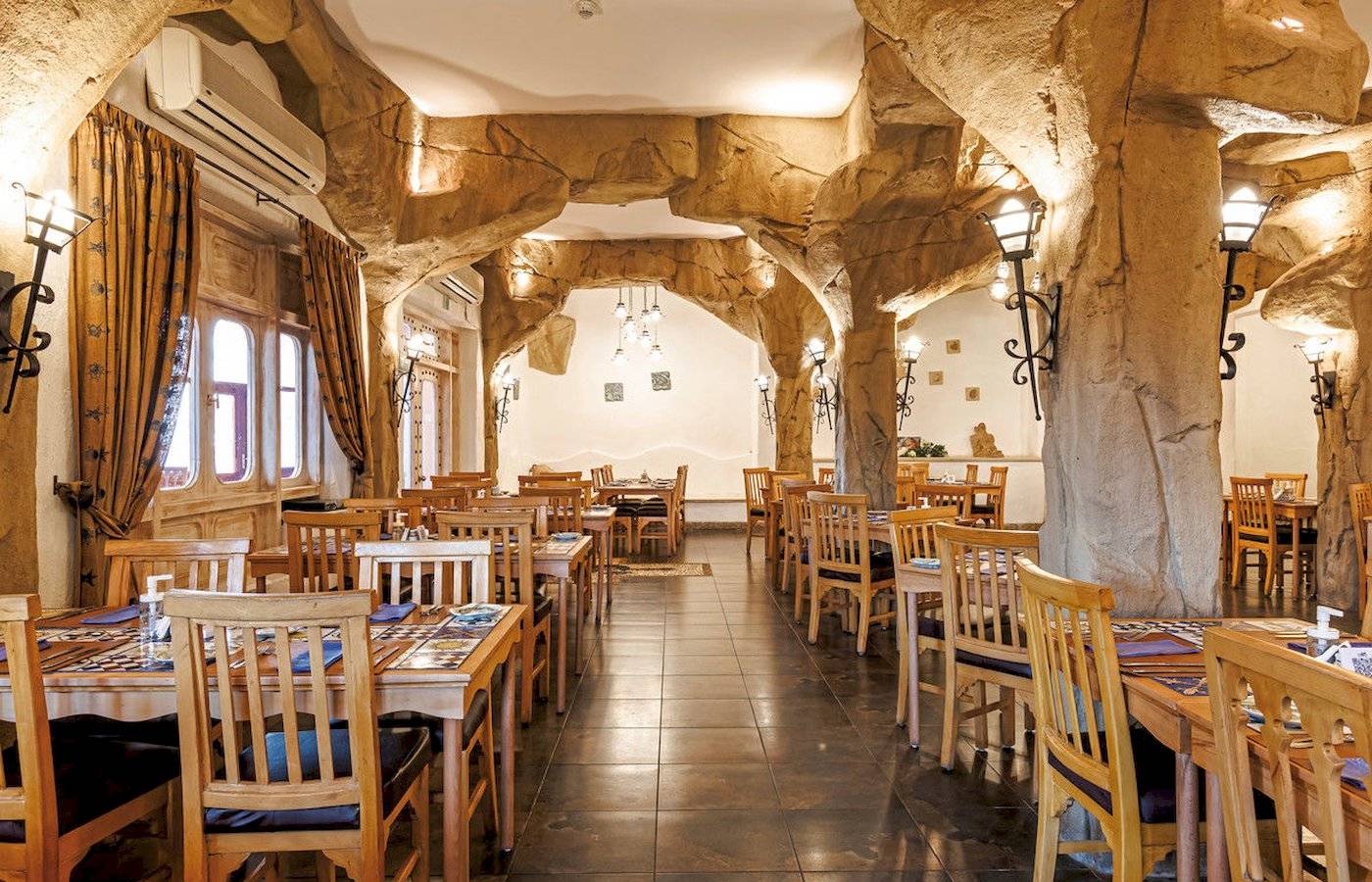 Innenbereich des Restaurants im SUNRISE Royal Makadi Resort mit Holztischen, Stühlen und steinernen Säulen.