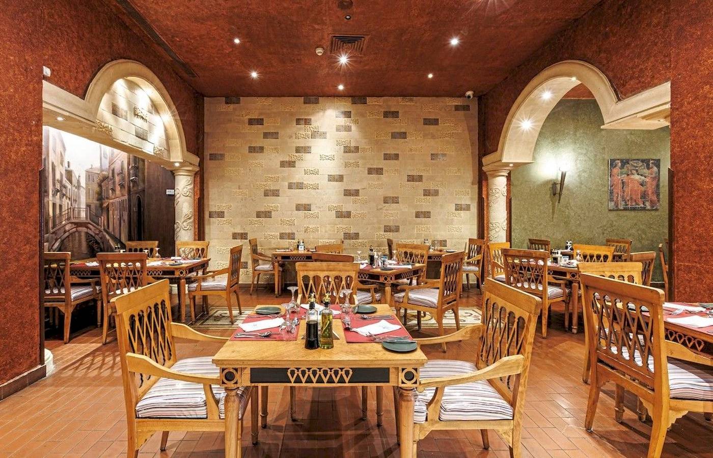 Restaurant im Sunrise Royal Makadi Resort mit Holztischen und Stühlen, gemusterten Wänden und Deckenbeleuchtung.
