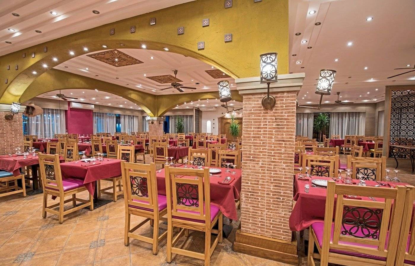 Innenbereich des Restaurants des Sunrise Royal Makadi Resort mit gedeckten Tischen, Holzstühlen und gemusterten Kissen.