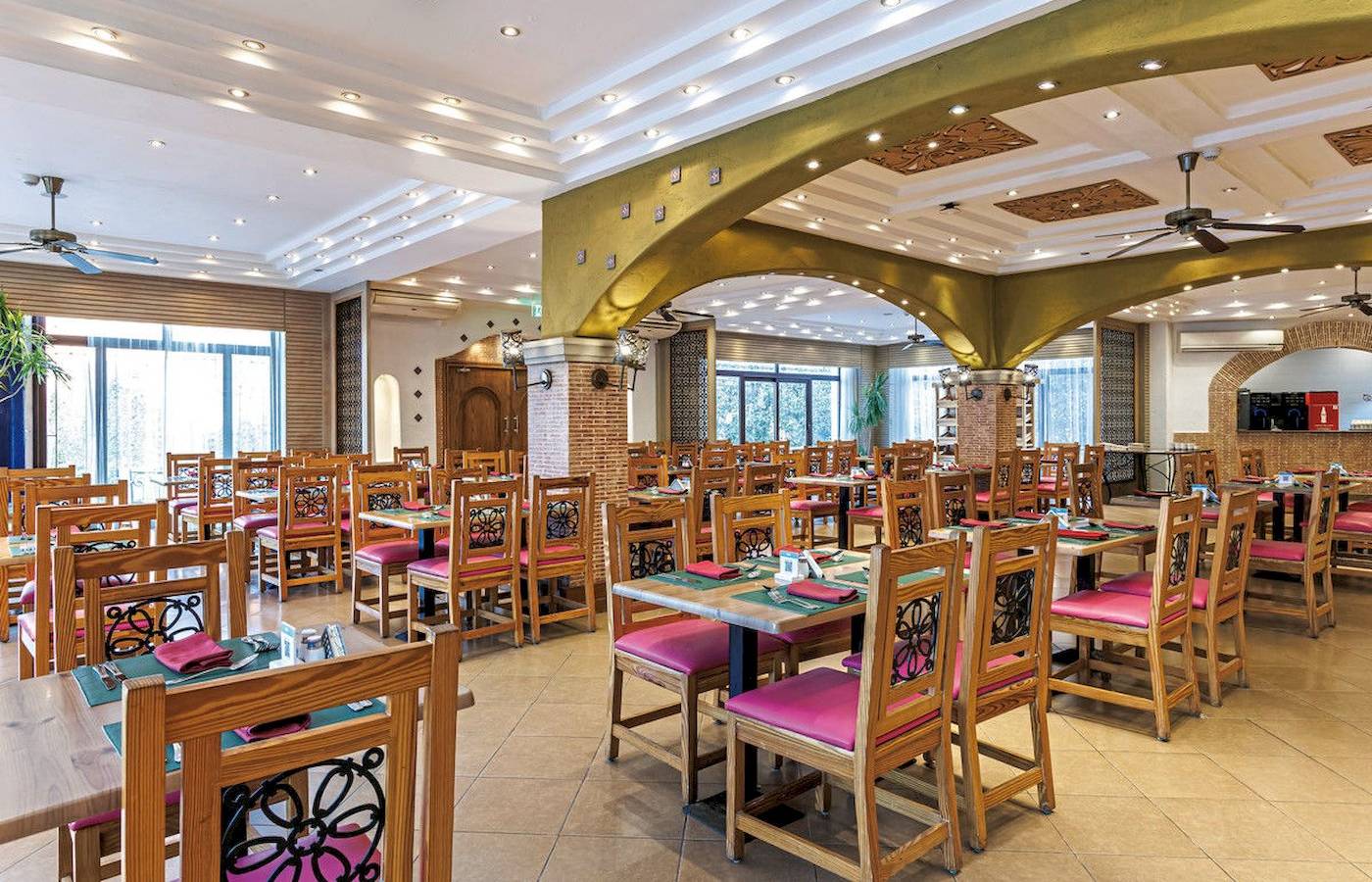 Innenbereich des Restaurants im Sunrise Royal Makadi Resort mit Holztischen und Stühlen, Deckenventilatoren und beleuchteten Decken.