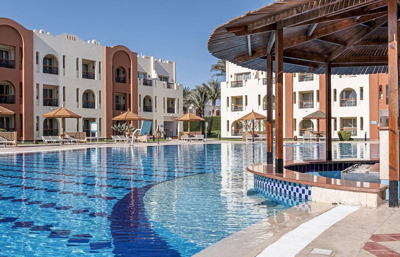 Pool-Bereich des Sunrise Royal Makadi Resorts mit umliegenden Gebäuden und Sonnenschirmen.