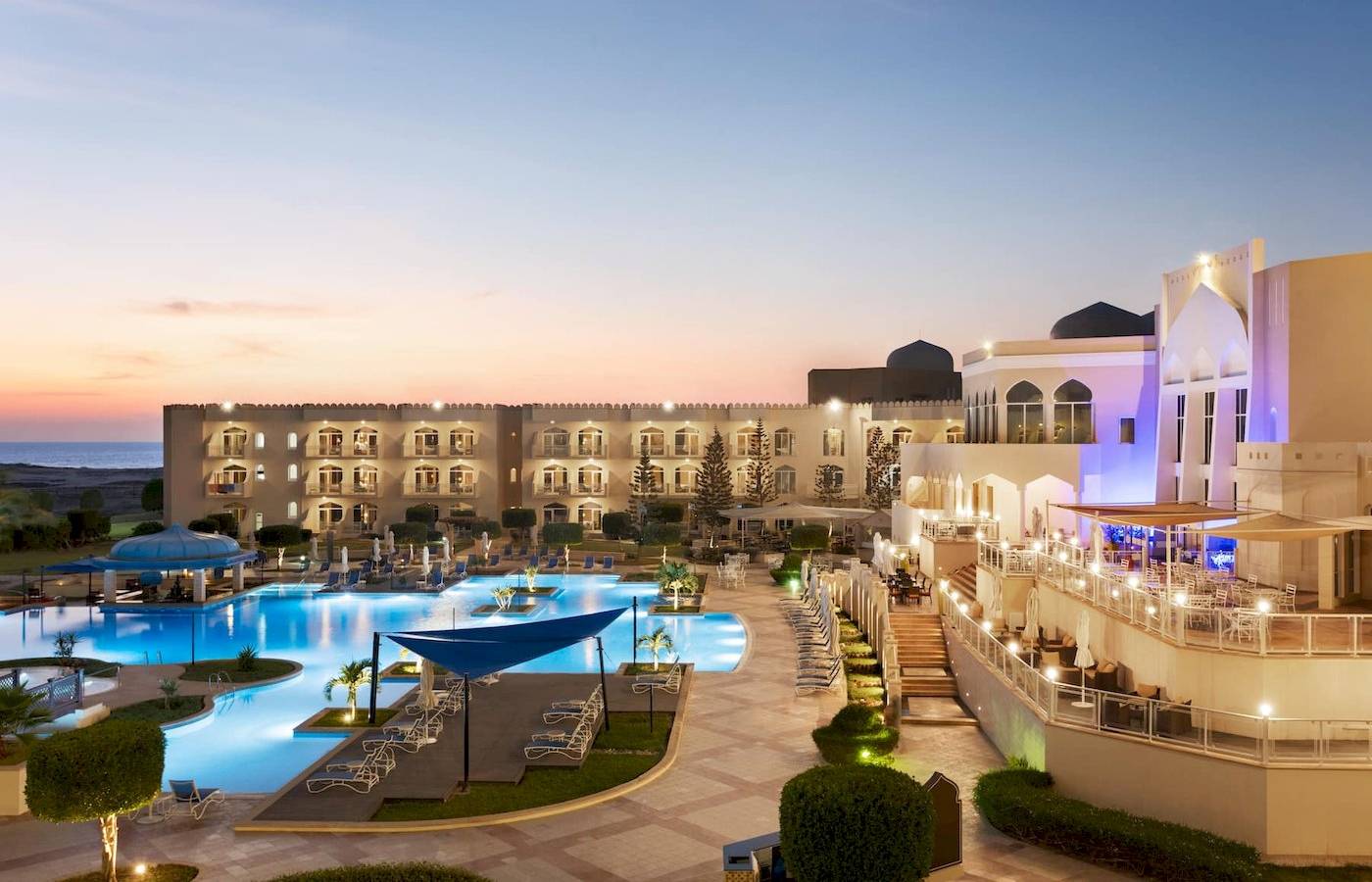 Abendliche Sicht auf das Wyndham Garden Salalah Mirbat Hotel mit Swimmingpool und Terrasse.