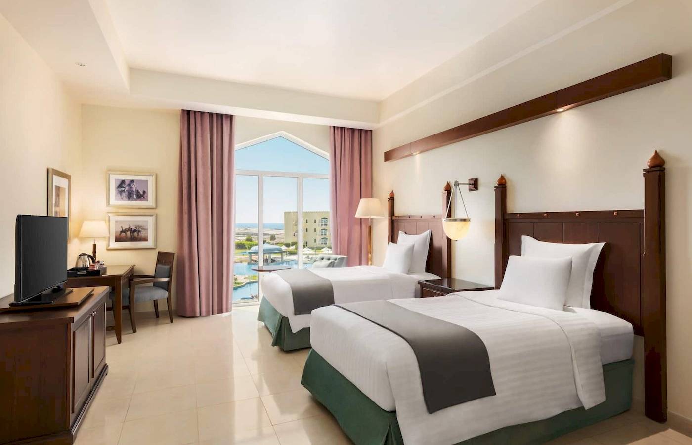 Doppelzimmer mit Meerblick im Wyndham Garden Salalah Mirbat Hotel, mit zwei Betten, Fernseher und Tisch, sowie ein großer Fenster mit Poolsicht.