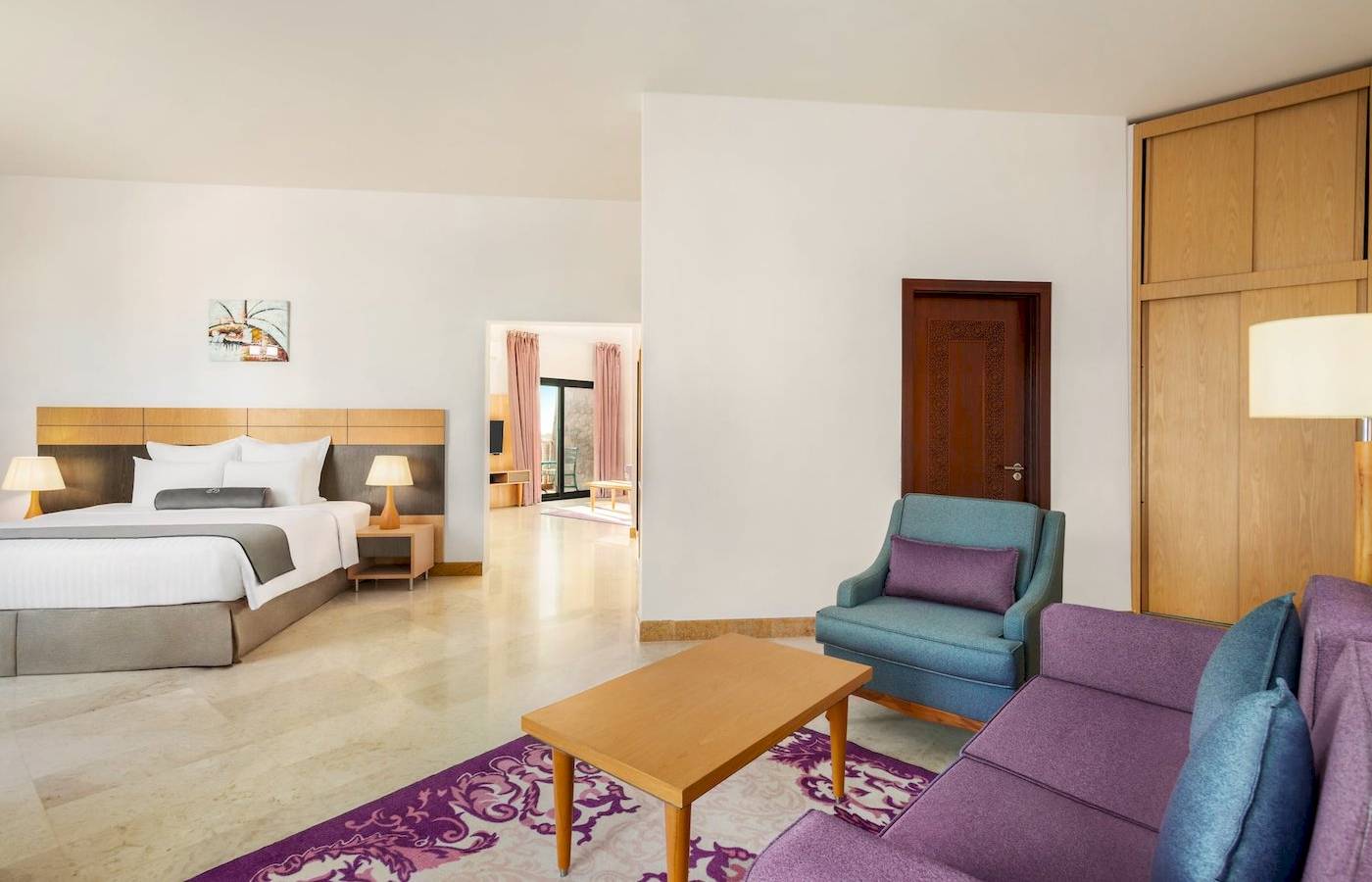 Schlafzimmer im Wyndham Garden Salalah Mirbat Hotel mit Doppelbett, Nachttischen, Lampen, Teppich und Wohnzimmermöbeln.