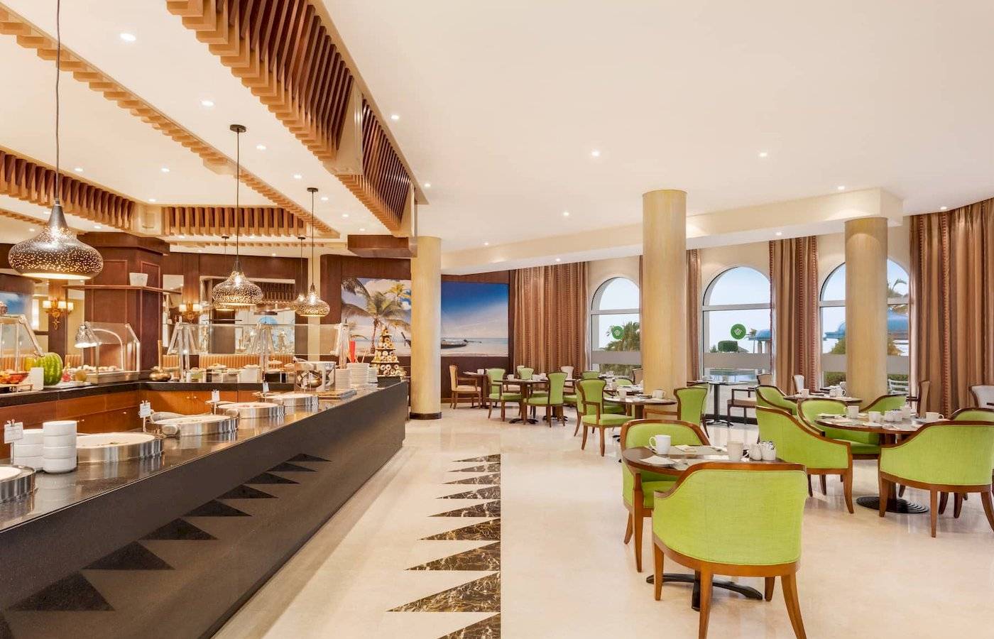 Innenbereich eines Restaurants im Wyndham Garden Salalah Mirbat Hotel mit grünen Stühlen und Tischen.