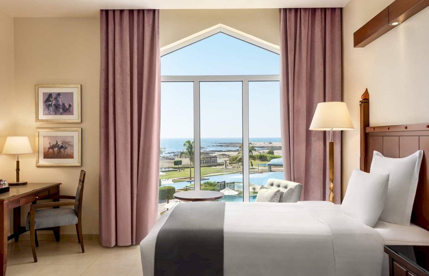 Zimmer im Wyndham Garden Salalah Mirbat Hotel mit Meerblick, großes Bett, Schreibtisch und Panoramafenster.