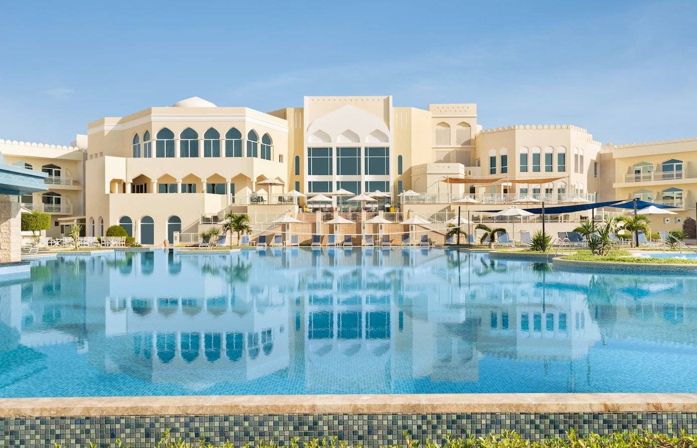 Außenbereich des Wyndham Garden Salalah Mirbat Hotels mit großem Pool und Sonnenschirmen.