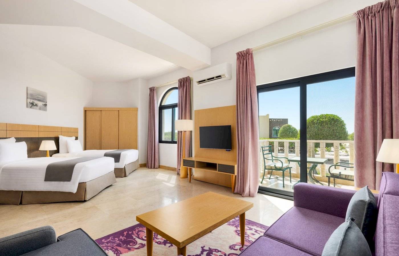 Wyndham Garden Salalah Mirbat Hotelzimmer mit zwei Betten, Fernseher, Tisch und Sofas.