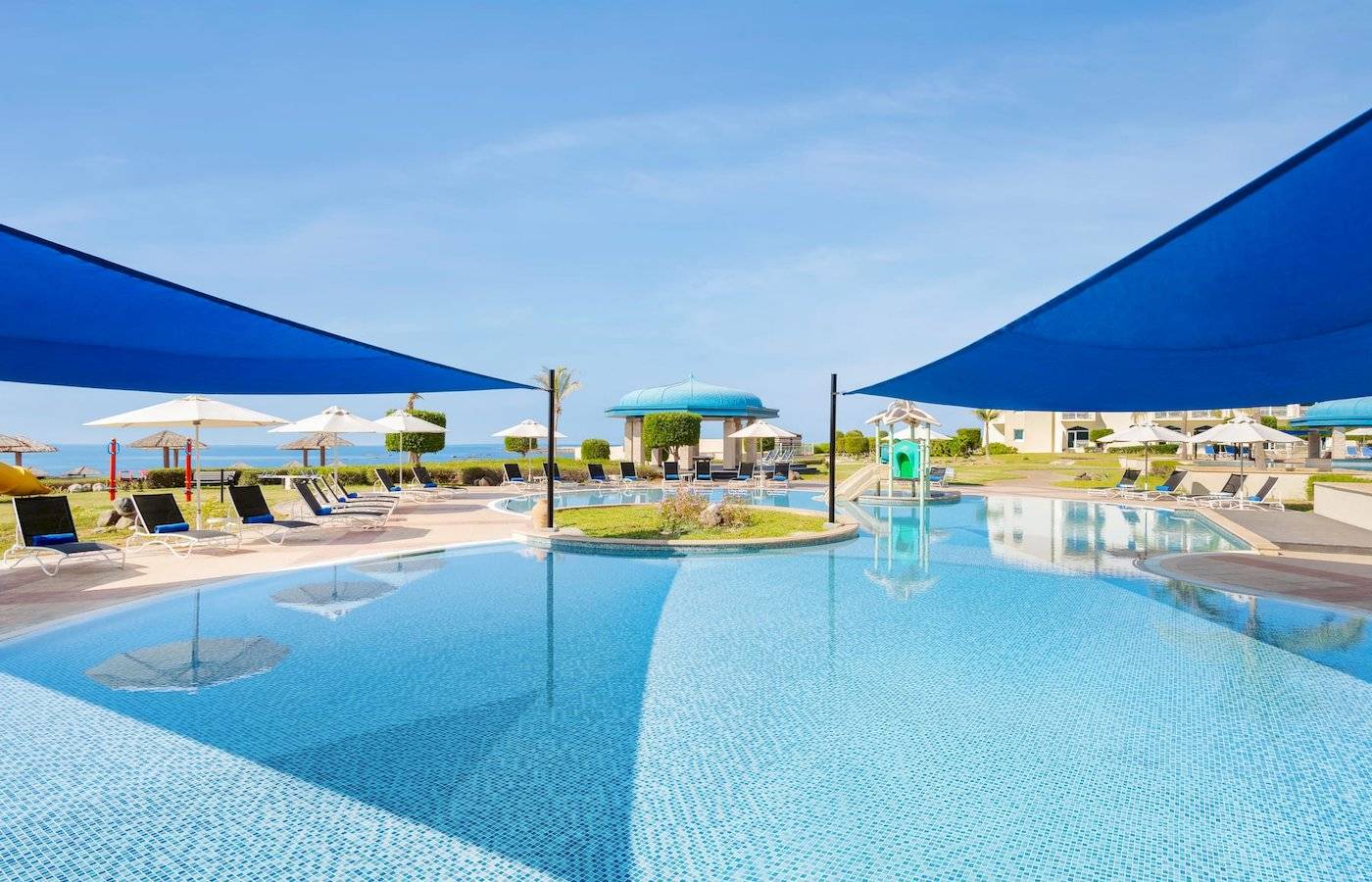 Außenpool des Wyndham Garden Salalah Mirbat Hotels mit Lounge-Stühlen und Sonnenschirmen