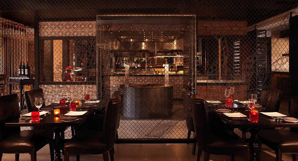 Innenbereich des Restaurants im Anantara The Palm Dubai Resort mit gegrillten Tischen und dunkler Atmosphäre.