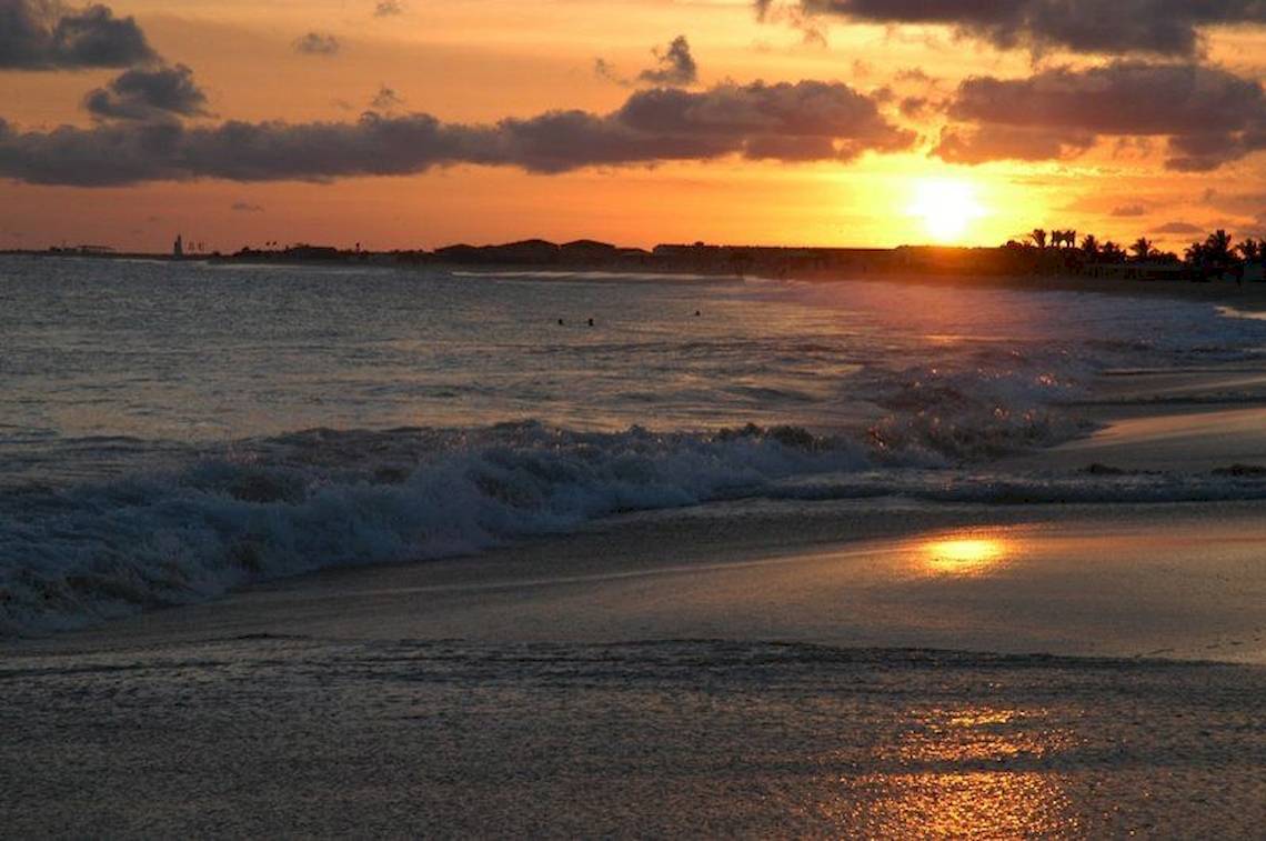 Sonnenuntergang am Strand mit Wellen, die auf den Strand treffen.