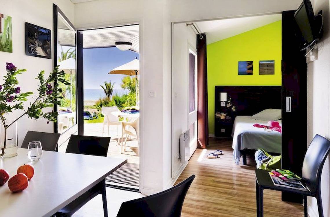 Innenansicht des Belambra Club Golfe de Lozari Hotels mit Wohnbereich, Esstisch und Blick auf die Terrasse.